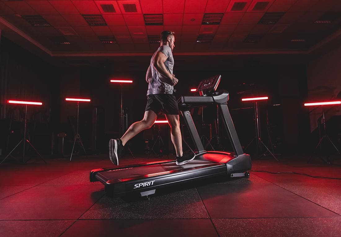 Athlete running on a treadmill in a dark gym with red lighting